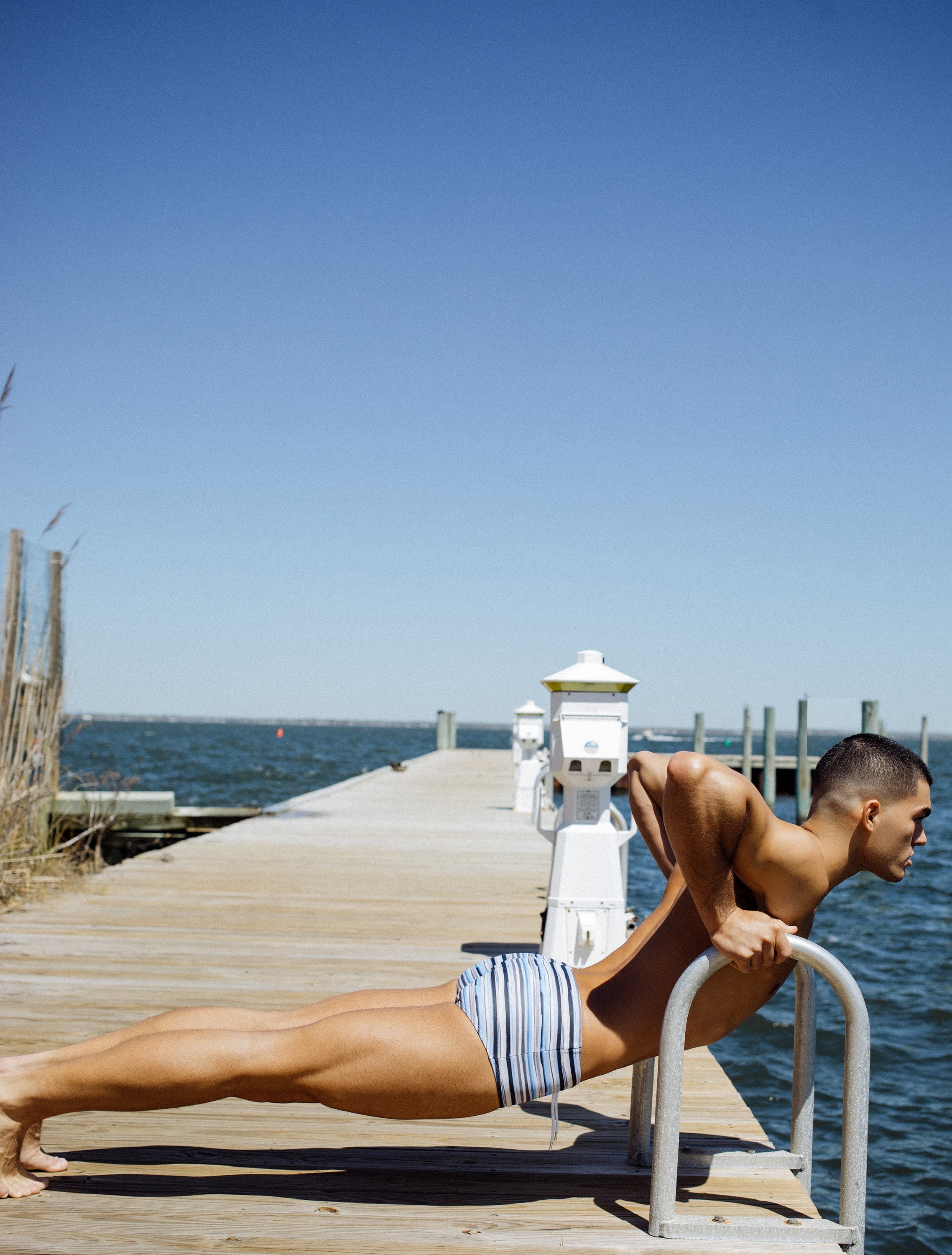Man doing push-ups on a pier wearing Parke & Ronen Striped print "Corcovado" swim brief in blue.